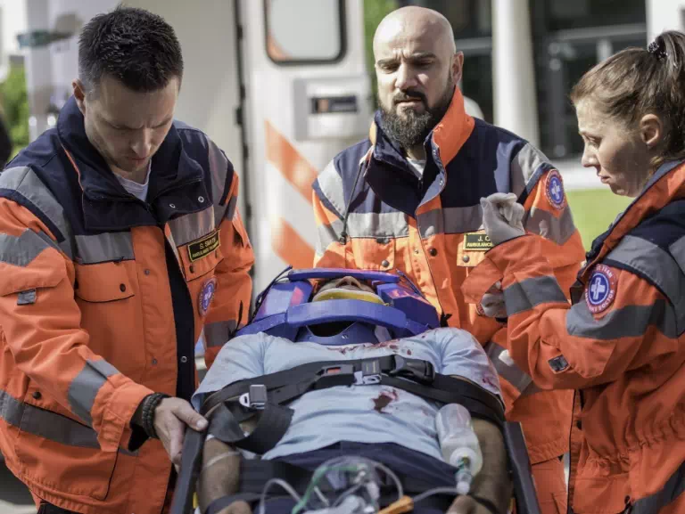 ratownicy medyczni stojący nad mężczyzną w stabilizacji na noszach